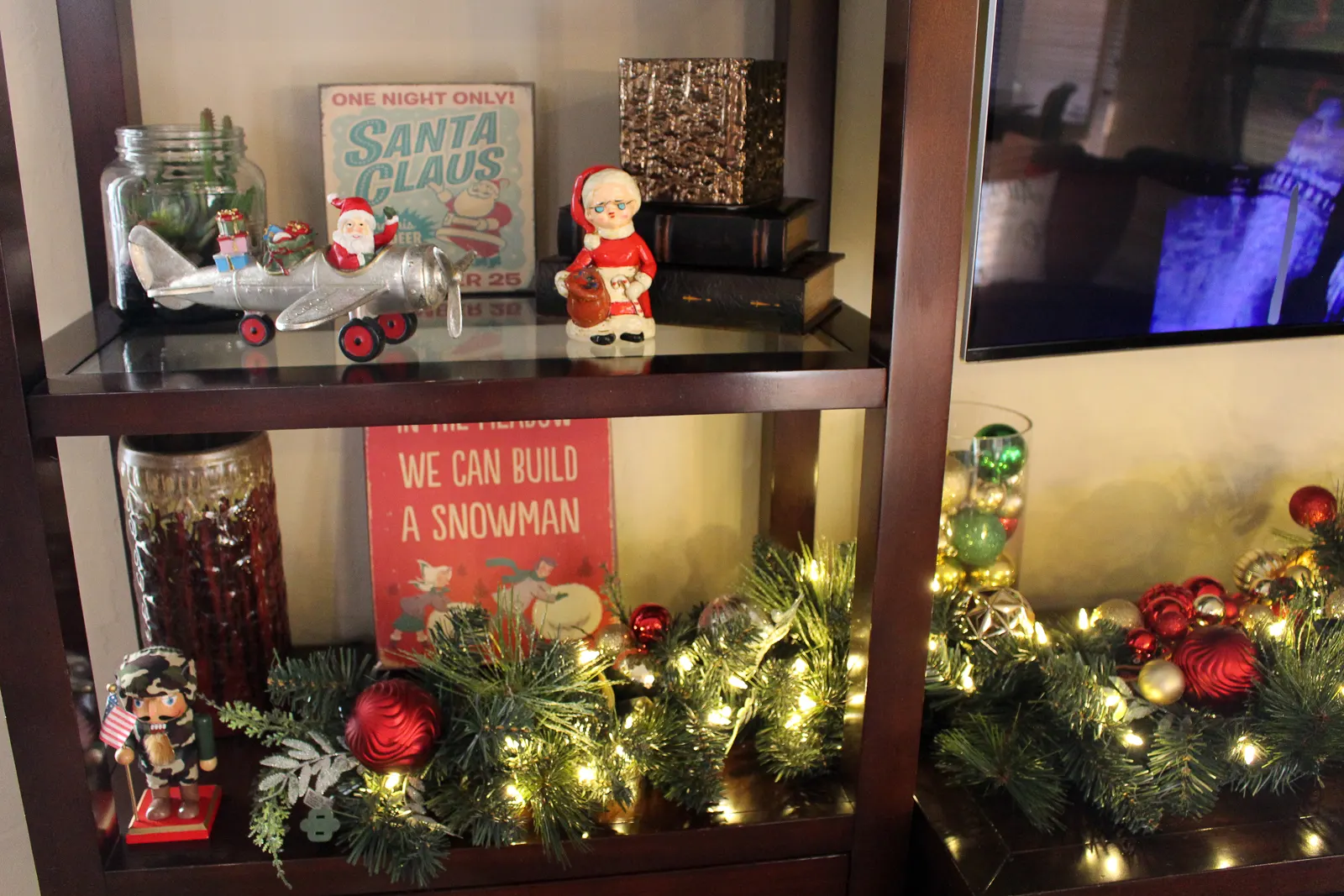 Holiday decorations on an entertainment center, including vintage Santa figurines and an illuminated garland