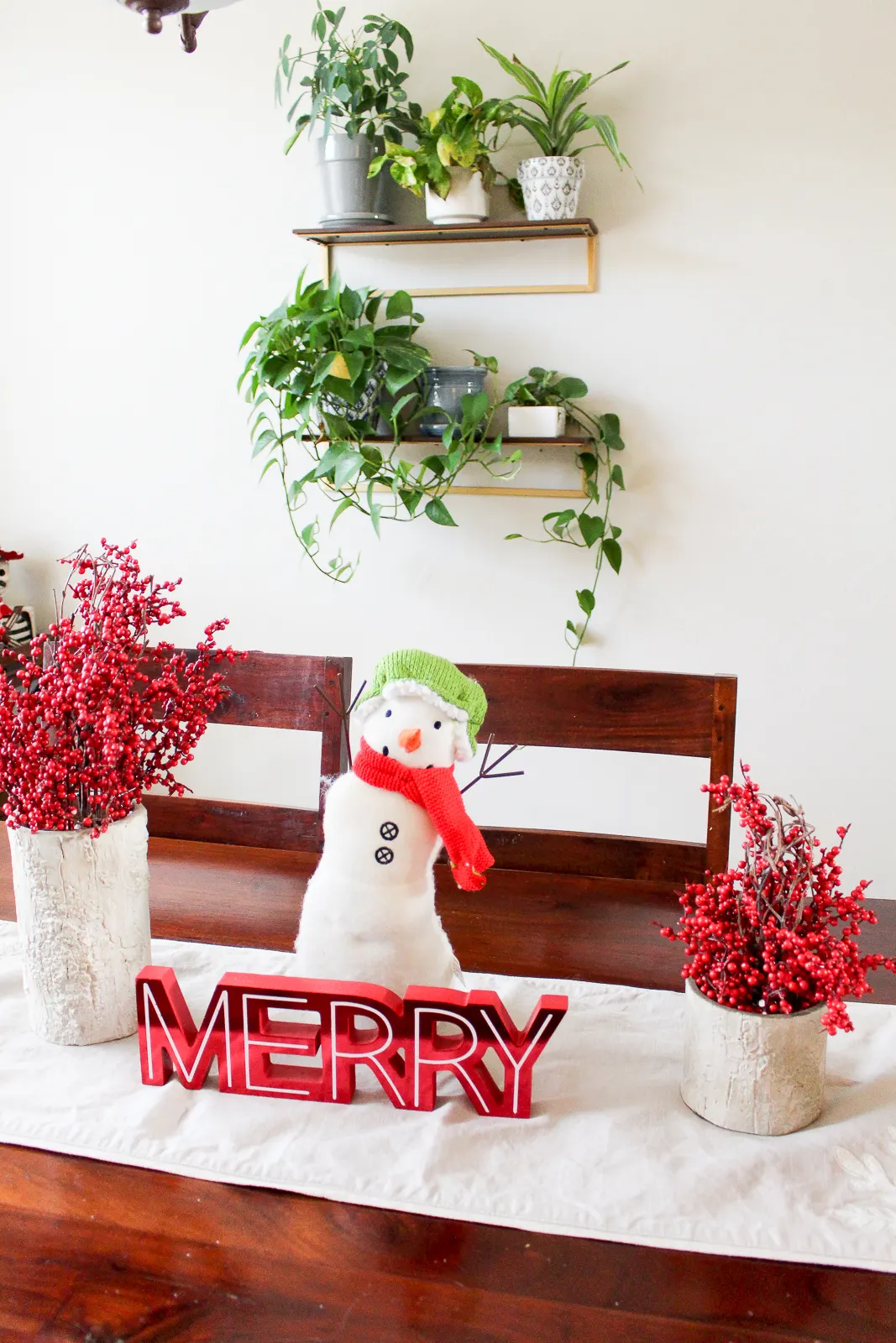 Holiday decoration of snowman on dining room table with two cranberry centerpieces and a sign that says Merry